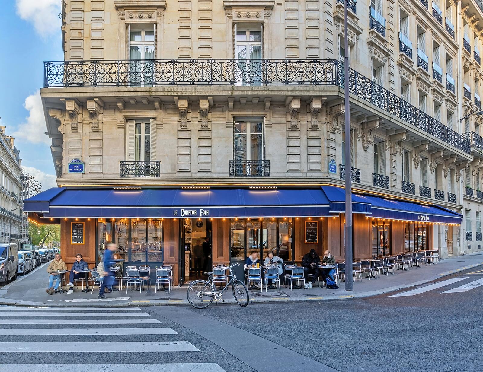 Vue intérieure depuis le comptoir du Comptoir Foch vers la baie vitrée, lumière ambrée et verres alignés au crépuscule